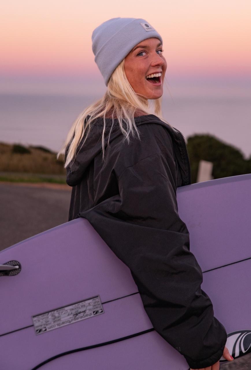 Katrīna Krūze with her surfboard at sunset